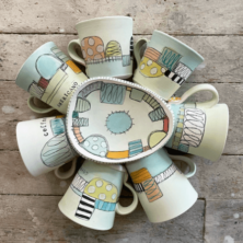Seven painted mugs and a bowl in the middle.